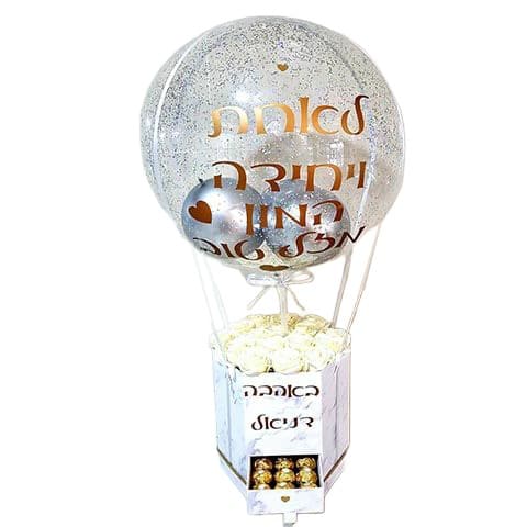 בלון שקוף גדול עם כיתוב אהבה מעל מארז לבן ובו סידור בהיר ומתוקים